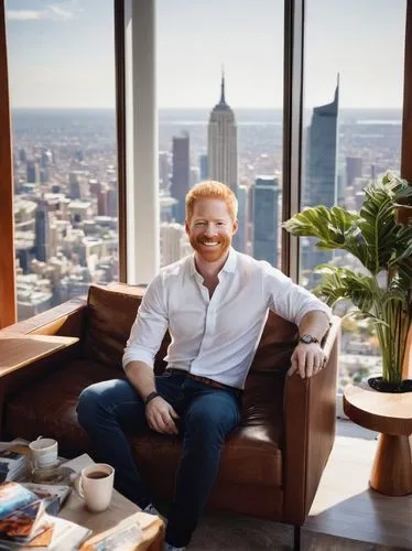 Jesse Tyler Ferguson, smiling, bright blue eyes, messy brown hair, casual wear, white shirt, dark jeans, sneakers, holding Architectural Digest magazine, sitting, relaxed pose, modern living room, lar