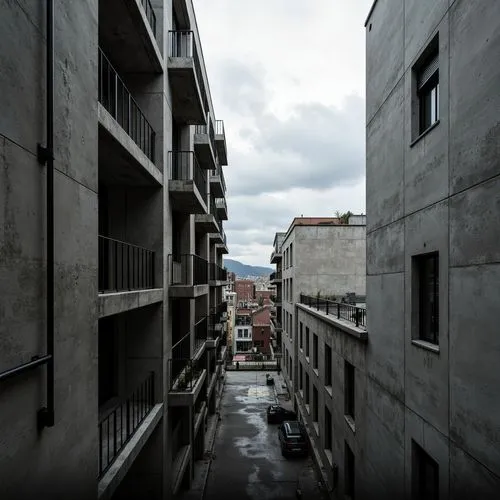 Exposed concrete walls, rugged textures, industrial pipes, raw steel beams, minimalist balconies, brutalist architecture, urban cityscape, gloomy overcast sky, dramatic shadows, high-contrast lighting