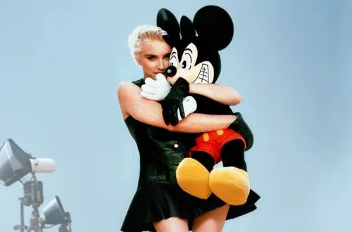 Madonna is on a movie set and she has Mickey Mouse on her shoulders. Madonna is wearing a sexy dress and has beautiful legs and she is wearing high heels. The movie set is full of crew members such as