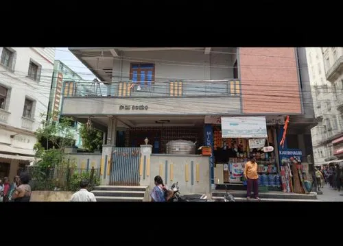 two people walking past a building in a city,shophouses,rathchaprasong,shophouse,jayanagar,triplicane,mithibai,bulandra theatre,prithvi,colaba,ramachandrapuram,matunga,ghatkopar,shivajinagar,bowbazar,