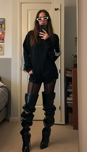 A young university student stands confidently in her bedroom, wearing a bold and casual urban outfit. She’s dressed in a black Adidas hoodie with white stripes running down the sleeves, paired with ma