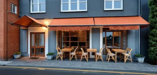 Facade of bakery. Walls color dark, terracotta. Glazing frames dark gray. Above the windows fabric awnings dark gray color. Lights are on in the windows and you can see the bread and baked goods insid