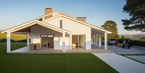 A modern, minimalist white house with clean lines and subtle stone accents on the facade. The porch features white beams and wooden flooring, adding warmth to the design. The house is slightly elevate