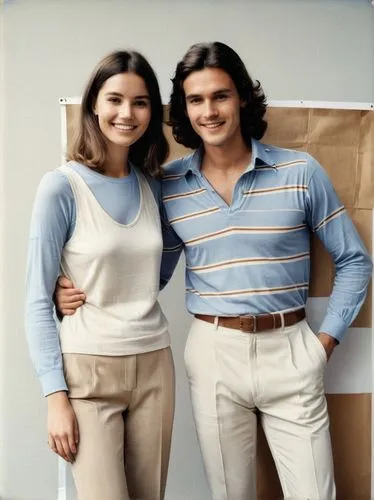 The picture shows two people, a young woman and an older man, posing amicably together. The young woman is on the left and is wearing a beige/white outfit consisting of a sleeveless top and trousers. 