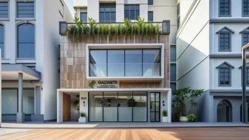 a 2 storied commercial building with light grey acp cladding and tinted grey glass for the windows. Railing on the terrace with some plants. A large wooden door on the ground floor left hand side.  ,C