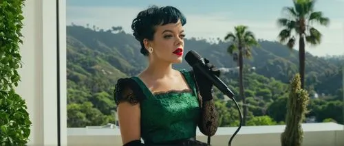 Lily Allen, British singer, blonde curly hair, bright red lipstick, vintage-inspired outfit, lace gloves, high-waisted skirt, black boots, holding a microphone, standing in front of David Harbour's mo