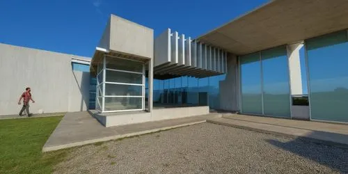 AREA DE CONVIVENCIA, CON PERGOLAS DE CONCRETO, LOSA CON REMATE DE VIGA DE ACERO, ESPEJO DE AGUA ,a person in a brown jacket walking past an unusual building,corbusier,epfl,corbu,siza,eisenman,snohetta