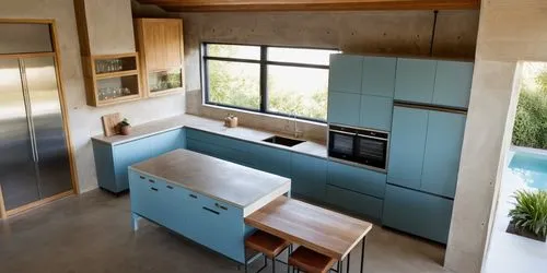 Kitchen with light blue shade doors, combined with an island with country-style  oak doors. Exposed concrete walls and ceiling, travertine floor, windows with garden and pool views. The general appear