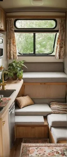 Modern travel trailer, cozy interior, beige walls, wooden floor, comfortable sofa bed, pillows in earth tones, small kitchenette, white cabinets, marble countertops, sink with golden faucet, microwave