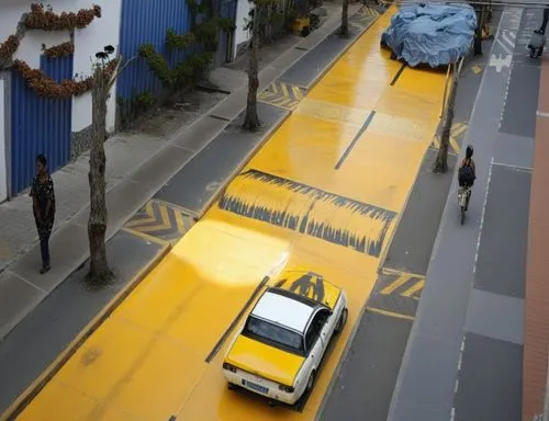 resalto en la calle amarillo 
el unico elemento amarillo es el resalto
calle de concreto gris
zonas verdes con vegetacion 
caminos peatonales con personas ,reductor de velocidad,bus lane,road marking,