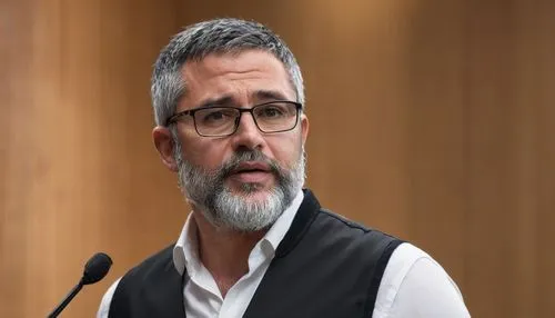 Titan speaker, middle-aged man, strong facial features, short black hair, small beard, glasses with silver frames, white shirt, black vest, formal trousers, microphone in hand, standing on a stage, sp