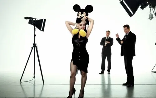 Madonna is on a movie set and she has Mickey Mouse on her shoulders. Madonna is wearing a sexy dress and has beautiful legs and she is wearing high heels. The movie set is full of crew members such as