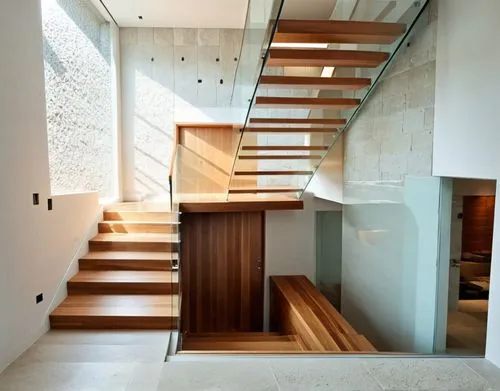 Tadao ando style beautiful staircase with teak wooden steps and elegant raining with light coming through a beautiful grid glass artic window wall on the side but solid stone wall at the back. The sta