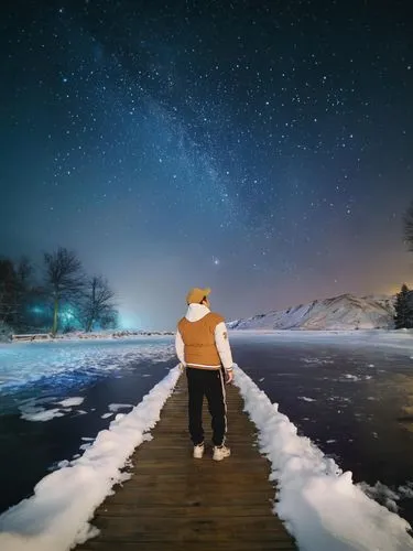 a man walks along a snow covered boardwalk beneath the stars,winter night,winter background,frozen lake,night photography,night snow,ice skating