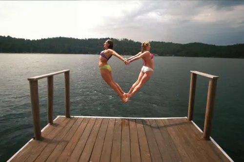 two women in bikinis stand on a pier,flying heart,floating over lake,watery heart