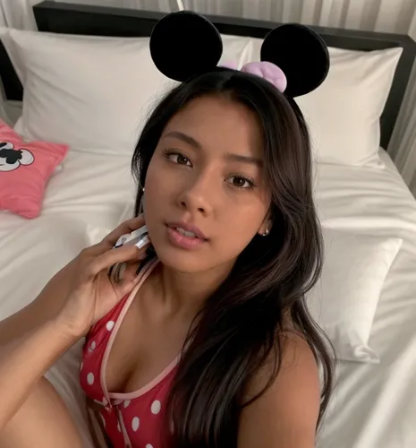 She is lying in bed in her simple room on her side.  She is wearing short Mickey Mouse pajamas and looking at her cell phone.,minnie mouse,minnie,janel,mouseketeer,micky mouse,jasmine sky,joi,filipina