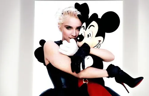 Madonna is on a movie set and she has Mickey Mouse on her shoulders. Madonna is wearing a sexy dress and has beautiful legs and she is wearing high heels. The movie set is full of crew members such as