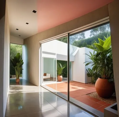 INTERIOR DEL VESTIBULO DE UNA CASA, QUE DA  AUN JARDIN INTERIOR CON MACETAS Y PLANTAS EXOTICAS, CANCALES DE ALUMINIO, CRISTAL, ILUMINACIÓN ELEGANTE Y TENUE,a house with a pink ceiling and two potted p