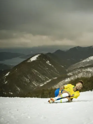 Neymar rolling from snowed top of mountain,man in yellow shirt laying on skis in snowy mountain area,hotham,whiteface,backcountry skiiing,carrabassett,neymar