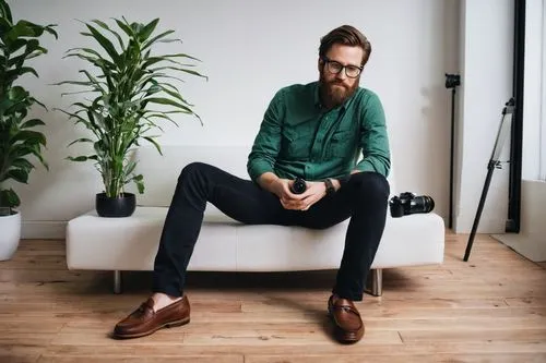 Interior design photographer, male, 30s, casual style, messy brown hair, black frame glasses, beard, white shirt, dark jeans, brown loafers, holding DSLR camera, studio strobe light, modern minimalist