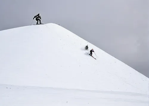 person skiing off the side of a large snowy side of a hill,ski mountaineering,ski touring,summit,backcountry skiiing,alpine climbing,snow cornice,mountaineering,skiers,snow mountain,cable skiing,climb