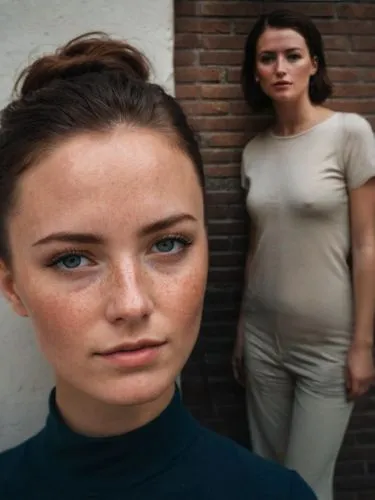 A woman with a neat hairstyle and freckles stands in front of a wall. A suitable male partner can be seen next to her.,two beautiful women standing together in front of a brick wall,vrouwen,vrouw,femk