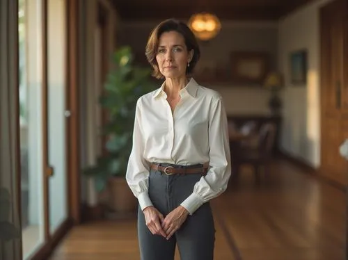 Thoughtful woman, mature lady, standing, hands clasped together, serious expression, minimal makeup, short brown hair, elegant white blouse, high-waisted dark grey pants, leather belt, black pumps, in