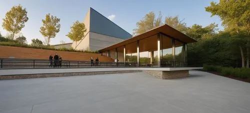 EXTERIOR DESIGN OF A DINING ROOM, LOCATED AT THE BACK OF AN INDUSTRIAL WAREHOUSE, BUILT WITH CONCRETE WALLS AND METAL ROOF, THE DINING ROOM HAS A SET OF STAGGERED STONE WALLS, A STAIR TO REACH THE LOW