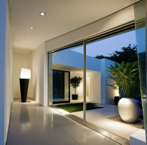 INTERIOR DEL VESTIBULO DE UNA CASA, QUE DA  AUN JARDIN INTERIOR CON MACETAS Y PLANTAS EXOTICAS, CANCALES DE ALUMINIO, CRISTAL, ILUMINACIÓN ELEGANTE Y TENUE,a large hallway has glass walls and floor,in