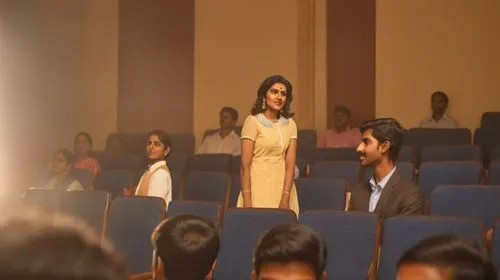 Renuka Chouhan as Amrita Kumaran stands up from her seat to volunteer rest of the audience watch her at awe, few young englishmen clap,student with mic,pgdm,vidya,neerja,tirunal,jntu,iilm,fddi,rajshri