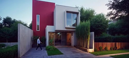 man walks through the backyard near a red and white modern house,modern house,prefab,inmobiliaria,smart house,vivienda,piramal