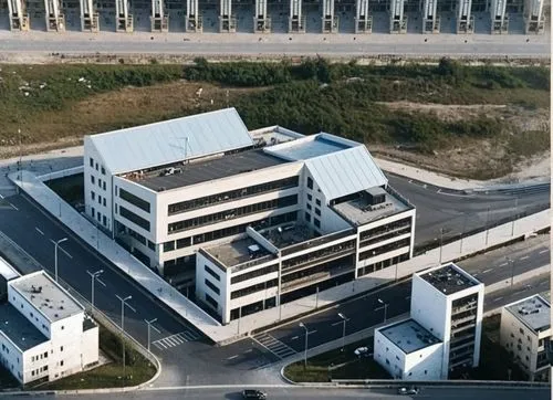 un edificio ubicado en una ciudad, su arquitectura esta basada en el constructivismo ruso. there are people and cars on the street.,a large white building next to two buildings,skolkovo,czarnuszka pla