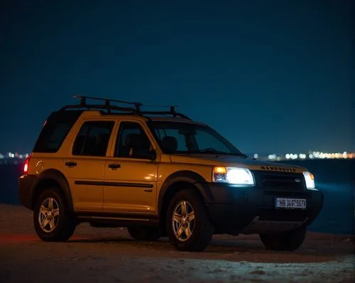 (High Definition HD) 2000 Land Rover freelander SUV 4x4w 3 door car decorated as a metallic mustard low car, parked by the sea at night.,an suv parked in front of a body of water at night,freelander,p