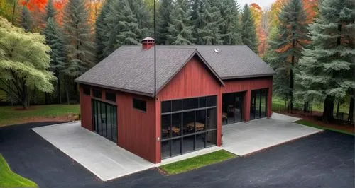 old red wood barn,  roof is dark  grey steel . Modern very large tinted windows. large trees in the background., a covered large stone patio with a roof and seating and BBQ located on the left side of