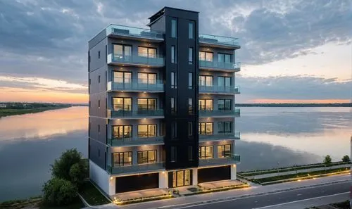 residential building near river.  . new paint outside. ground floor parking and few cars visible on wide road. glass railing and glass facade. grey and black exterior.,an apartment building in a resid