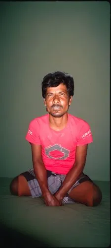 a man is sitting on the ground in front of a green wall,padmasana,manjeet,rajesh,chandraswami,kafeel,goundamani