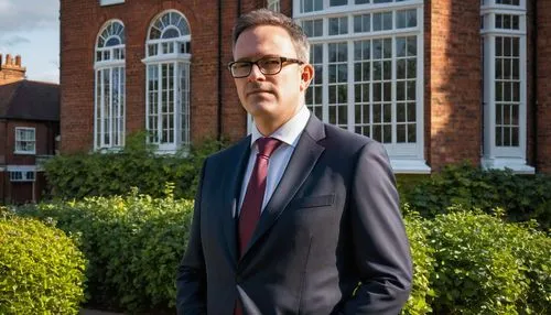 Middle-aged male architect, formal attire, glasses, short brown hair, clean-shaven, standing confidently, Bishop's Stortford town center, historic buildings, red-brick Victorian houses, greenery surro