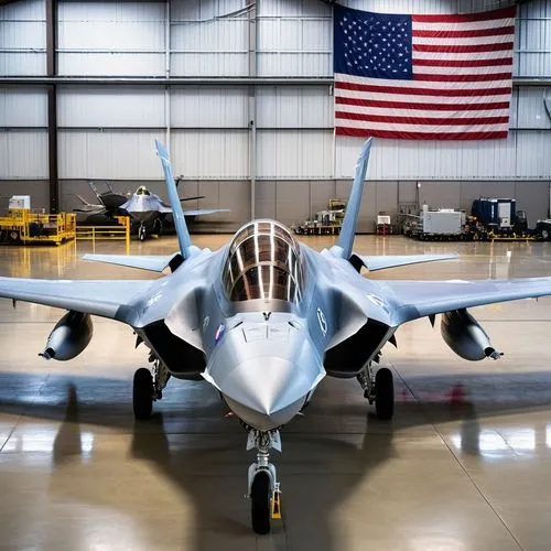 A Lockheed F-35 in two tone grey on upper sides is parked in a big fully equipped modern U.S. hangar with a poster mirroring the gorgeous female pilot together with the U.S. flag hanging on the wall, 