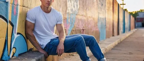 American, young adult, male, muscular build, short brown hair, bright blue eyes, slight stubble, casual wear, denim jeans, white graphic t-shirt, sneakers, leaning against, graffiti wall, urban citysc