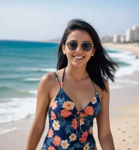 The 18-year-old Moroccan girl with black hair is walking with flip flops and a floral swimsuit by the sea in Tel Aviv.  She is wearing sunglasses and smiling,a woman is walking along the beach in her 