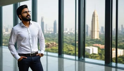 Modern Indian architectural firm, outsourcing company, young male architect (30yo), glasses, stylish beard, white shirt, dark jeans, black shoes, standing, gesturing, pointing, in front of a large flo