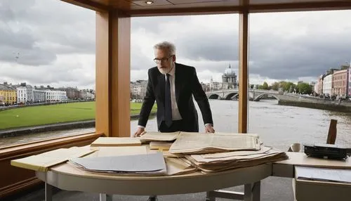 Modern Irish architectural design competition, solo judge, middle-aged man, glasses, grey hair, beard, black suit, white shirt, tie, holding a scale model, standing in front of a large wooden desk, pa