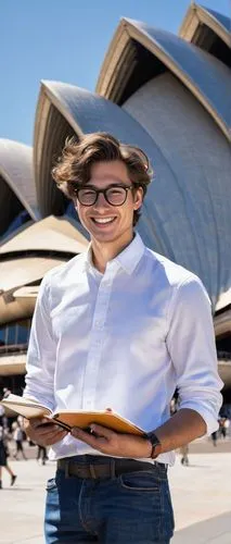 Male, young adult, bachelor of design architecture, USYD alumni, casual wear, white shirt, dark blue jeans, black sneakers, messy brown hair, glasses, smiling, holding a sketchbook, standing in front 