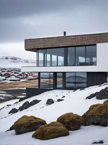 Icelandic architecture, Reykjavik cityscape, modern Nordic style, sleek lines, minimalist design, white concrete walls, large glass windows, wooden accents, snow-capped roof, rugged terrain, rocky out