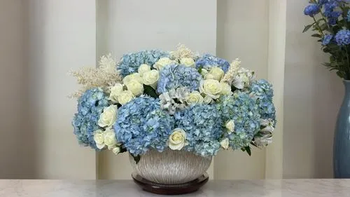 an arrangement of blue and white flowers sits in a silver vase,plate hydrangea,hydrangeas,flower arrangement lying,flower arrangement,floral arrangement,blue hydrangea