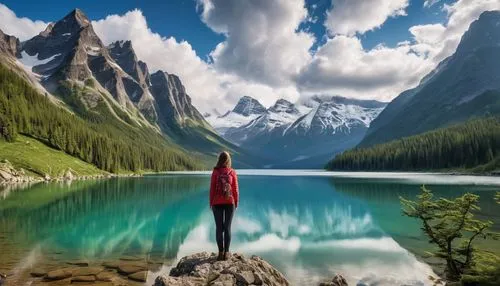 "A woman stands at the edge of a majestic mountain range, looking out over a breathtaking landscape of towering peaks and a serene lake below. The sky is filled with clouds that wrap around the mounta