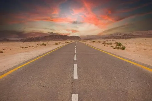 the long road is painted yellow and red as the sky looks ominous,road of the impossible,road to nowhere,vanishing point,straight ahead,long road,open road