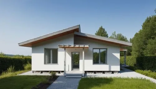 small modern house. The walls are white. Gray roof. There is a forest around the house.,a white house that is next to some trees,passivhaus,inverted cottage,electrohome,prefabricated buildings,arkitek