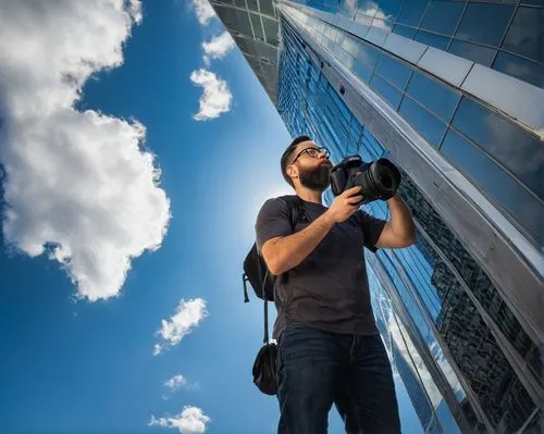 Professional photographer, male, 35yo, beard, glasses, casual clothing, holding DSLR camera, standing, looking up, admiring architecture, cityscape, skyscraper, modern building, glass and steel struct