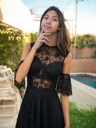 She is wearing a black lace dress, background is outside,social,little black dress,black and lace,black dress,quinceañera,black dress with a slit,in a black dress,a girl in a dress,vintage lace,black 